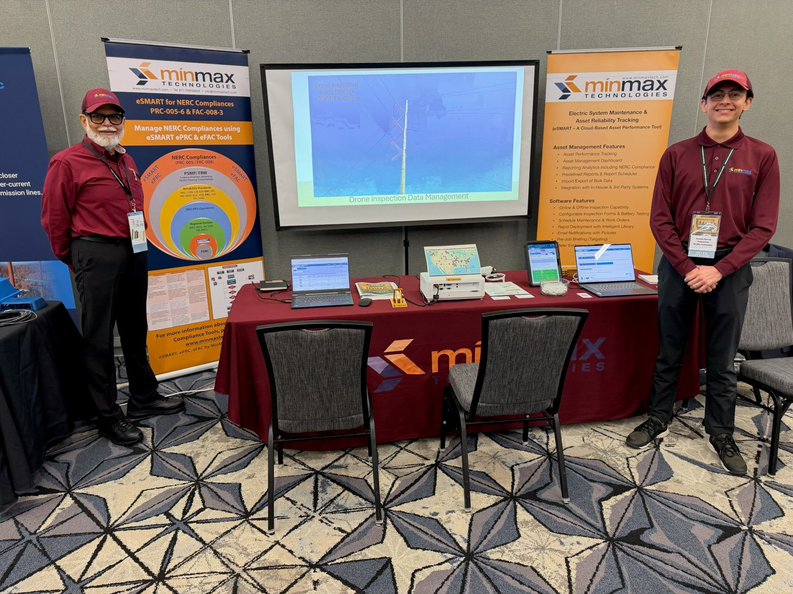 Two MinMax team members at the MinMax booth at the Midwest Transmission Conference, with a drone inspection demo on screen